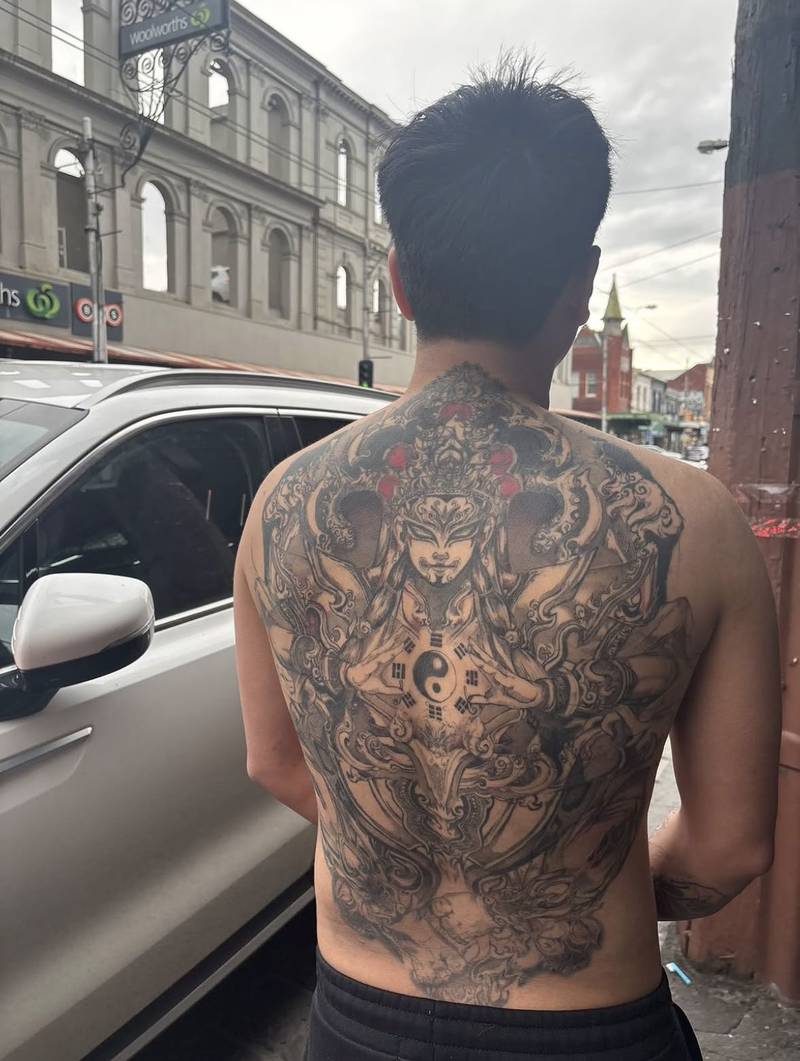 Completed tattoo across the back: an armoured figure in an ornate headdress holding a yin-yang symbol, surrounded by curling lines and red accents